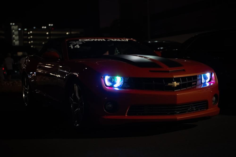 An orange Chevrolet Camaro at night with glowing blue headlight rings