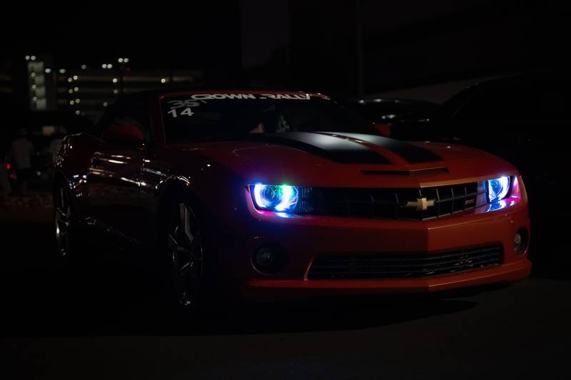 An orange Chevrolet Camaro at night with glowing blue headlight rings