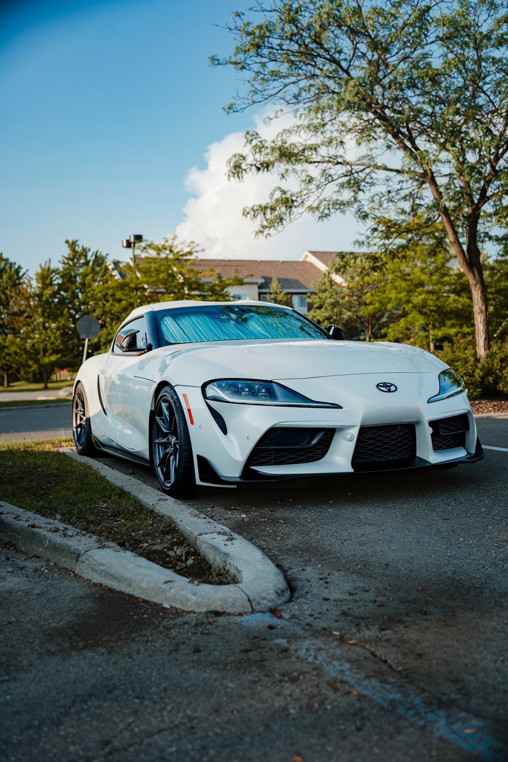 A white Toyota Supra parked at a curb under a blue summer sky