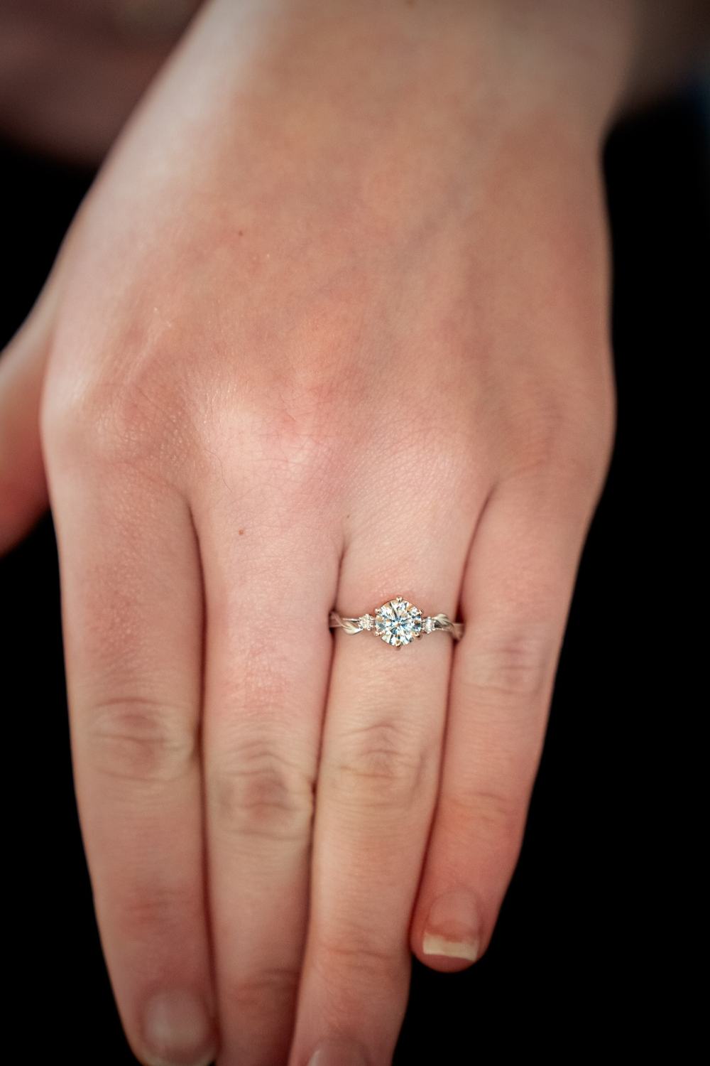 A hand wearing a diamond engagement ring against a dark background