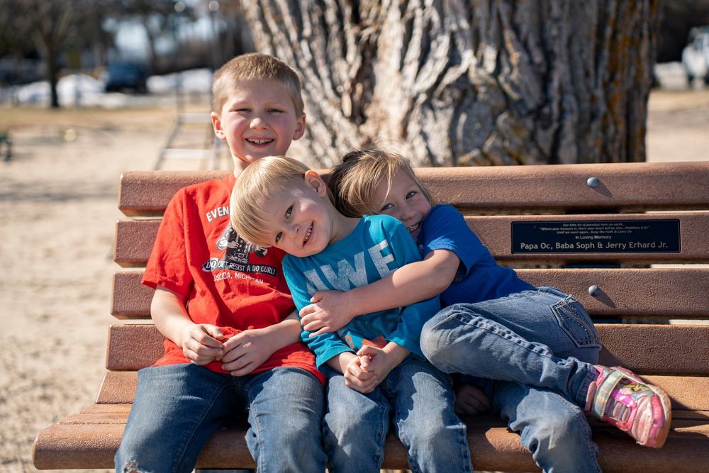 Three young brothers lean on each other and laugh on a park bench