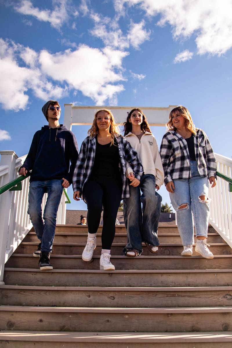 Four friends walk down a white wooden staircase under a bright blue sky