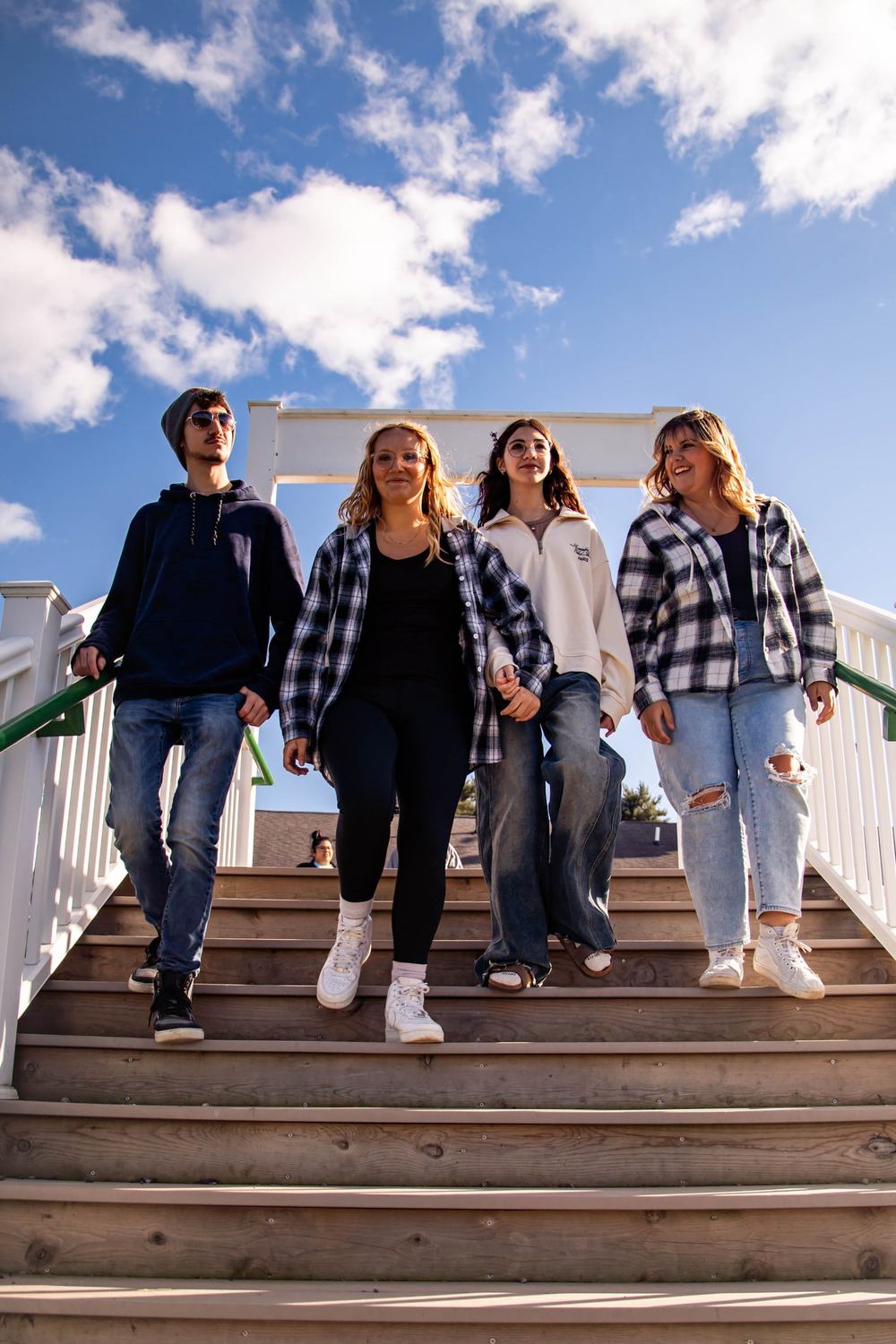 Four friends walk down a white wooden staircase under a bright blue sky
