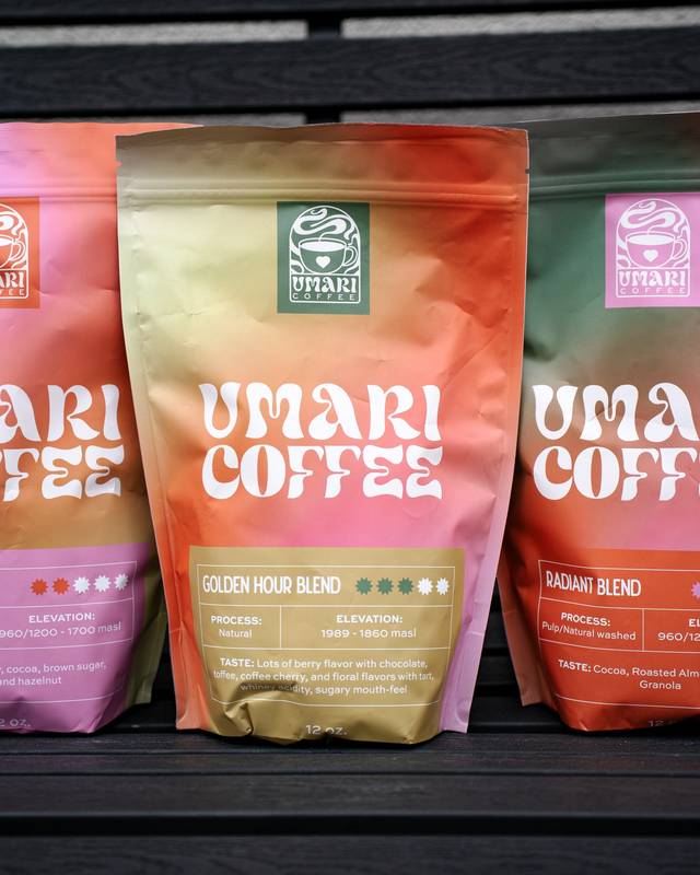 Three gradient coffee bags in pink, gold and orange standing on a dark wooden bench
