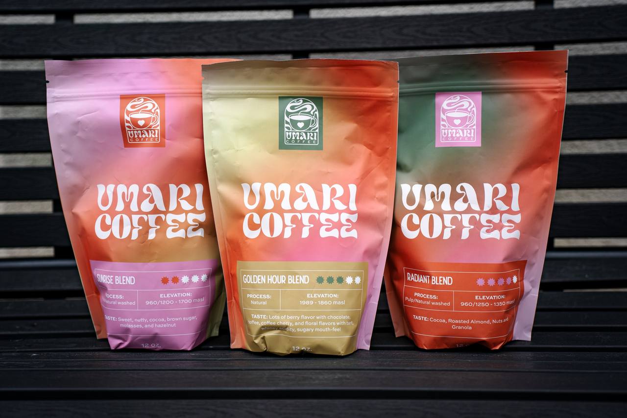 Three gradient coffee bags in pink, gold and orange standing on a dark wooden bench