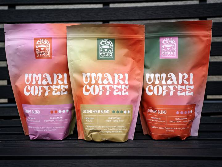 Three gradient coffee bags in pink, gold and orange standing on a dark wooden bench