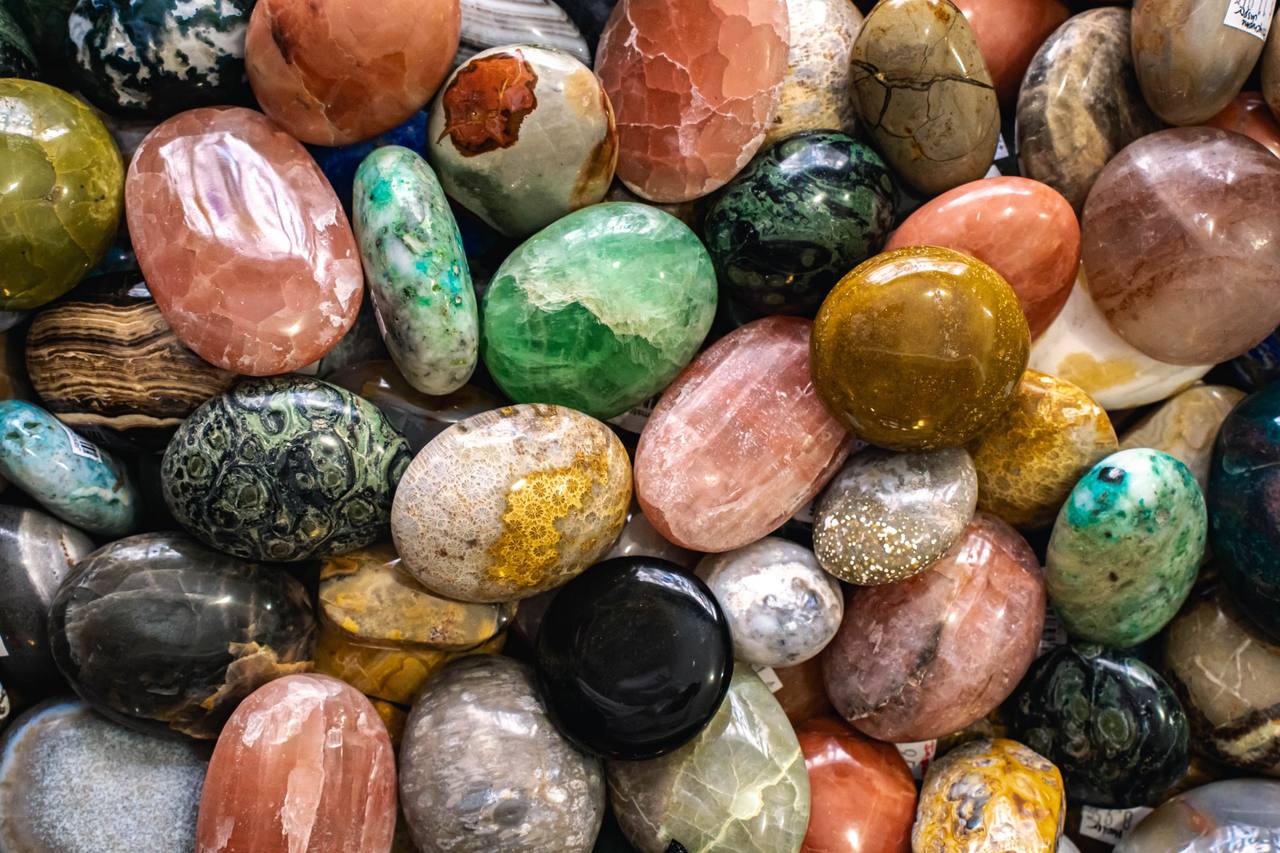 A colorful pile of polished palm stones in greens, pinks and golds