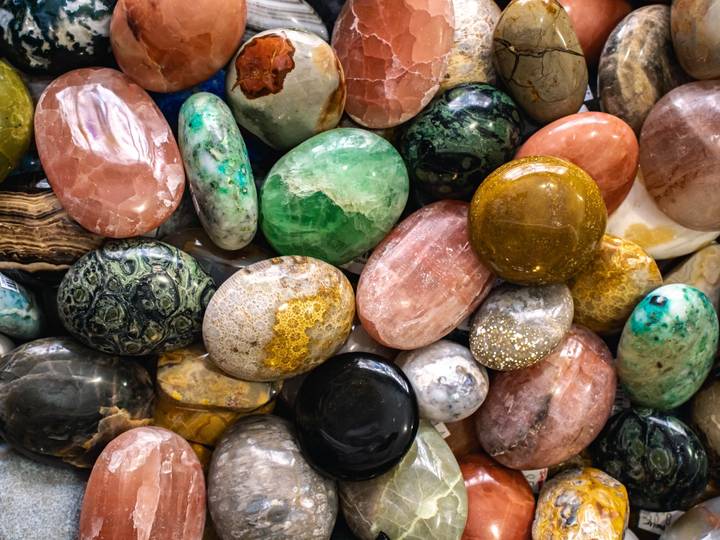 A colorful pile of polished palm stones in greens, pinks and golds