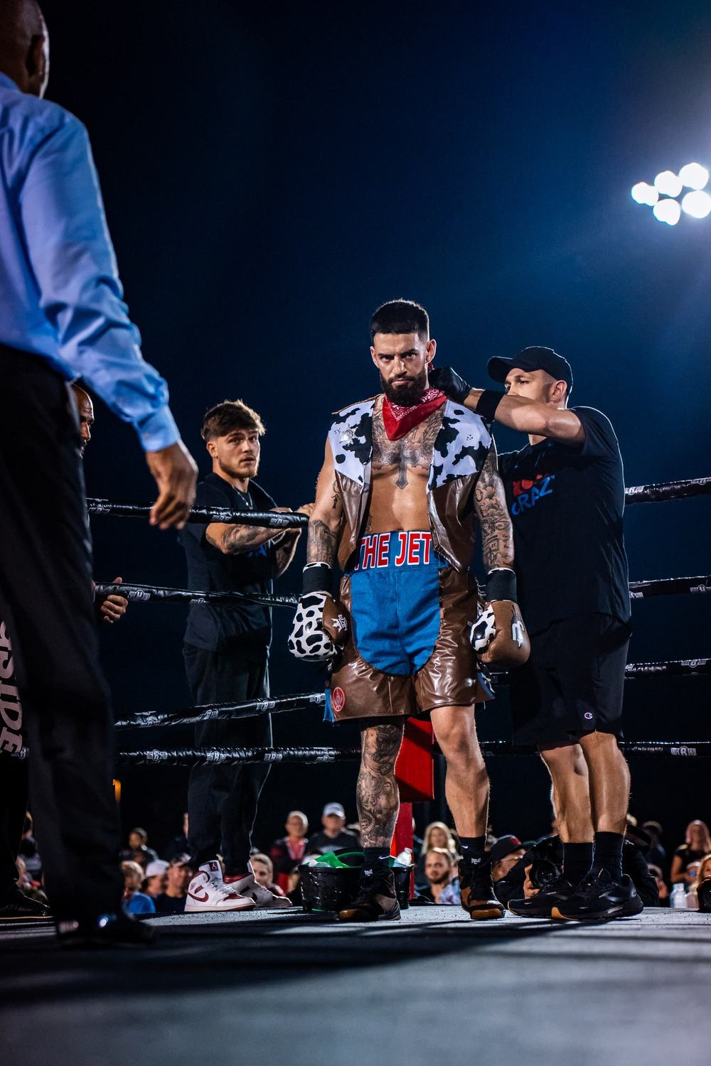 A boxer in a red bandana stands in the ring with his team under the lights