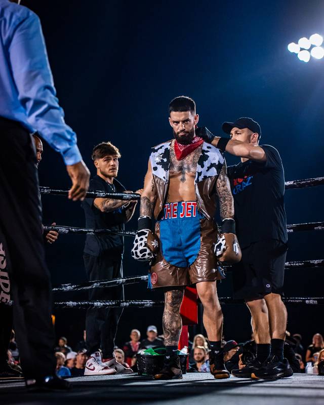 A boxer in a red bandana stands in the ring with his team under the lights