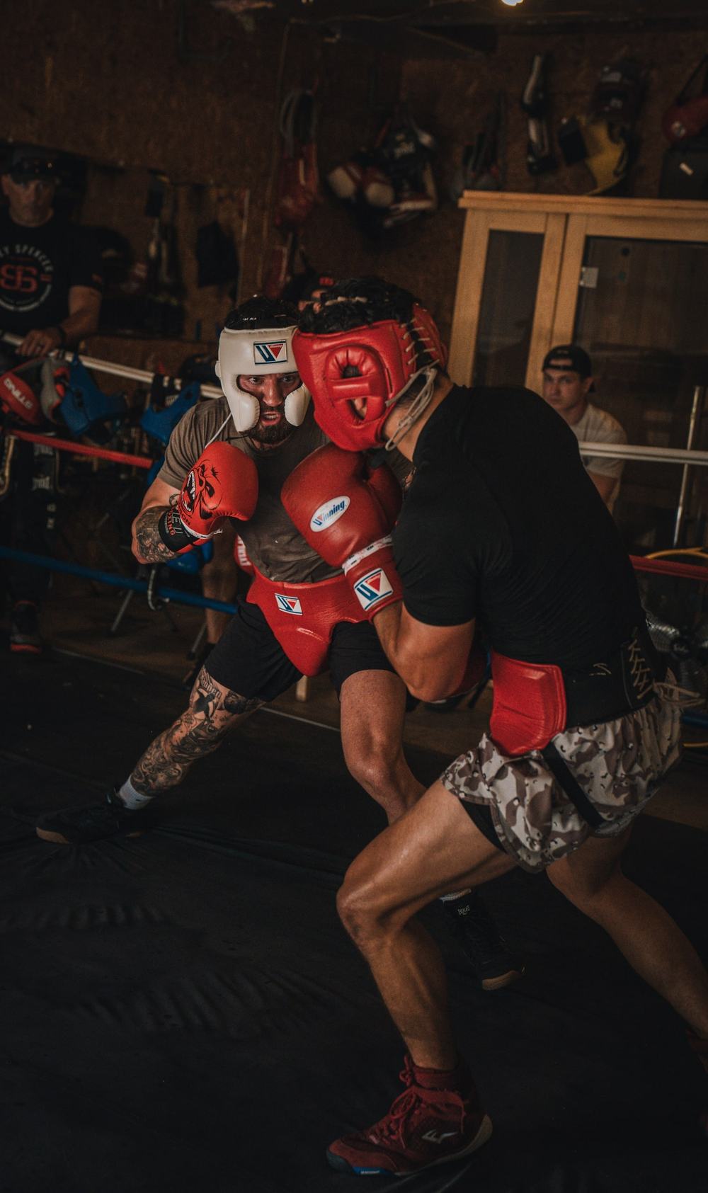 Two fighters in headgear clinch in a dim boxing gym