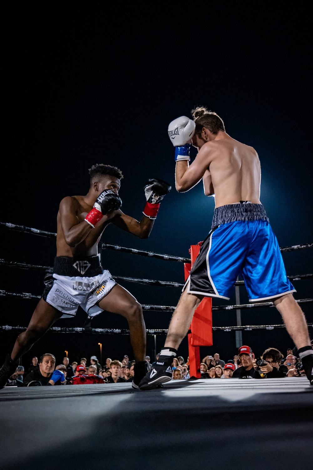 Two boxers exchange punches in the ring under a dark sky