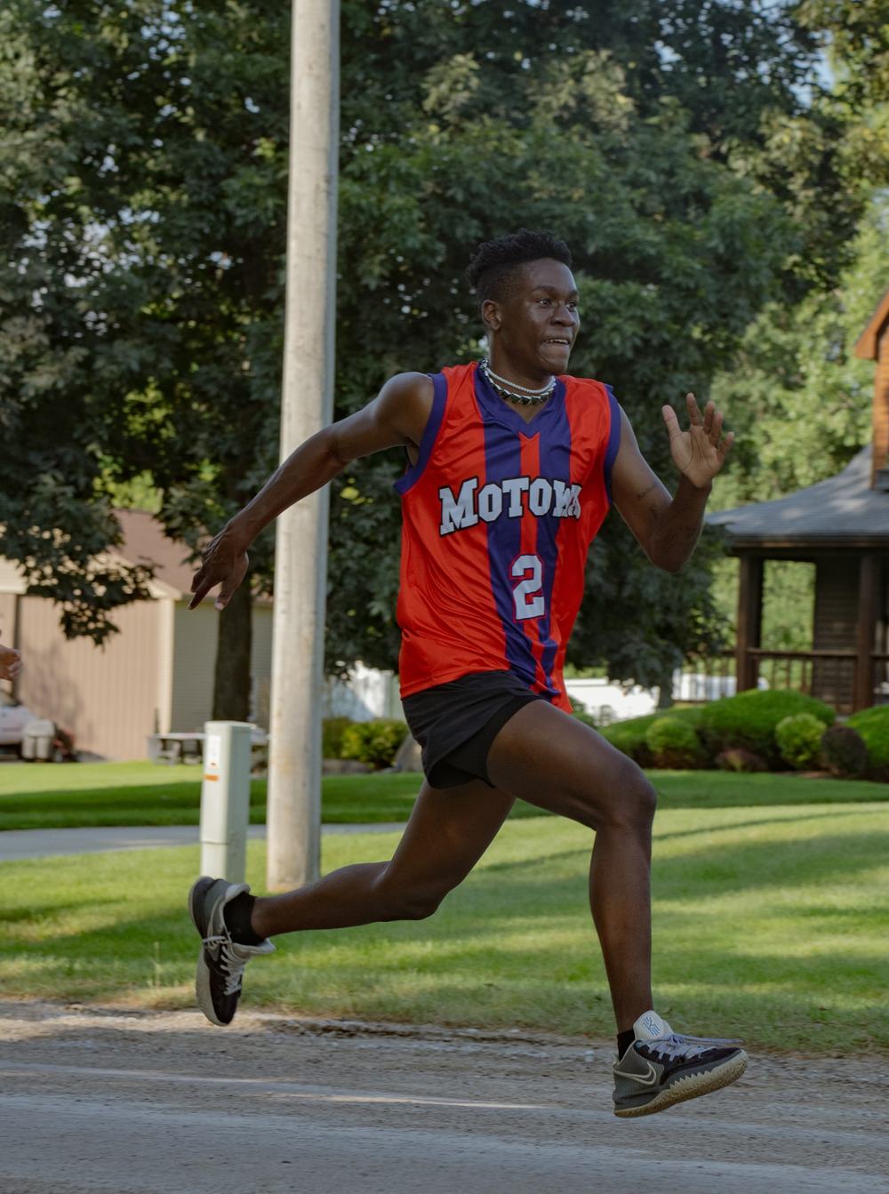 A runner in a red and blue Motown jersey mid-stride on a tree-lined street